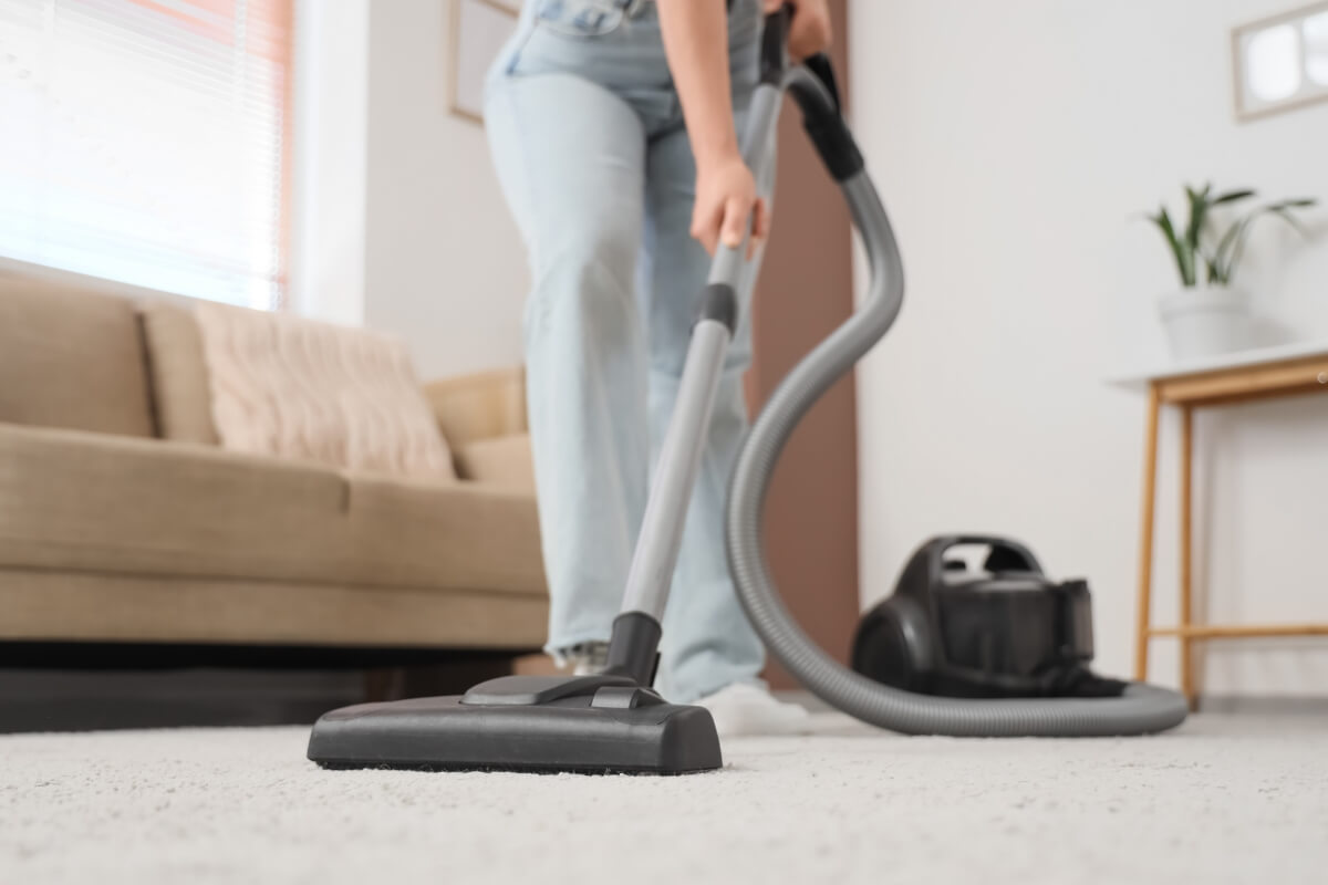 A low-angle shot of a person vacuuming a light-colored carpet in a living room.