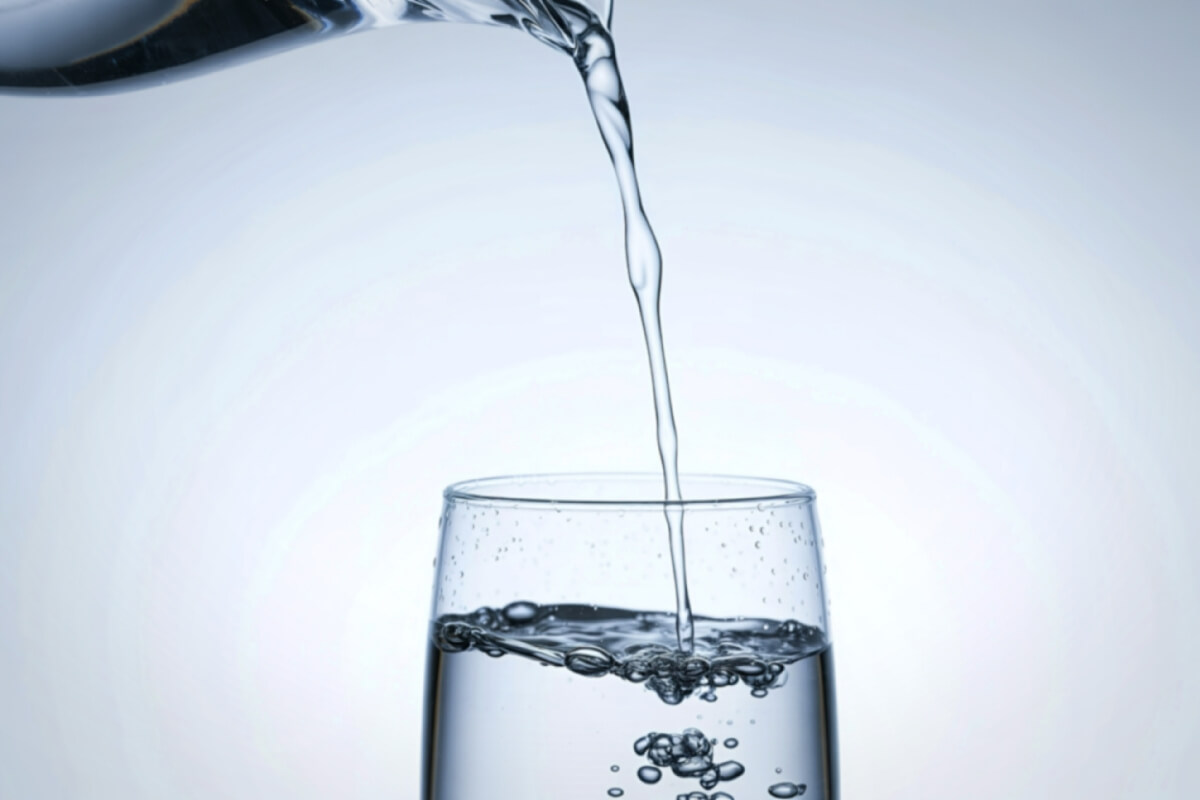 A clear stream of water being poured from a pitcher into a glass.
