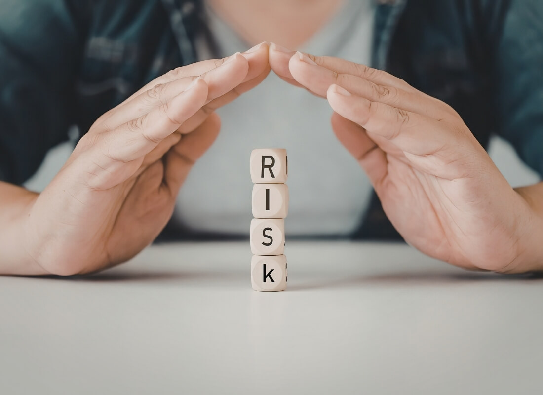 Hands cupped protectively over a stack of wooden blocks that spell out the word "RISK".