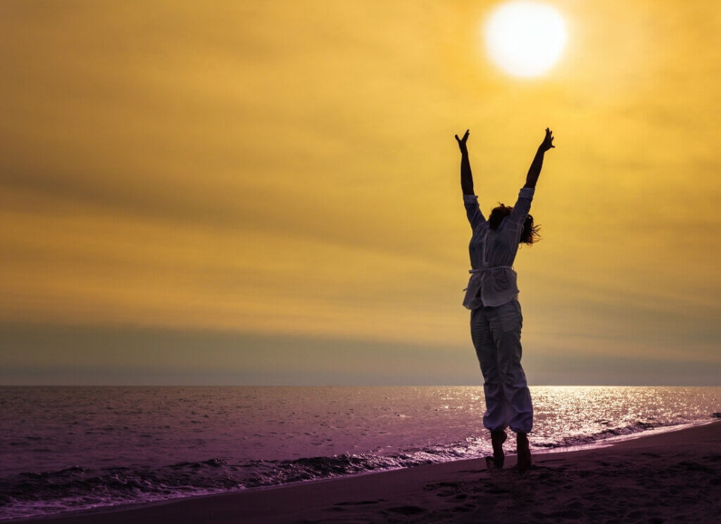 Silhouette of a person jumping for joy on a beach during a golden sunset.