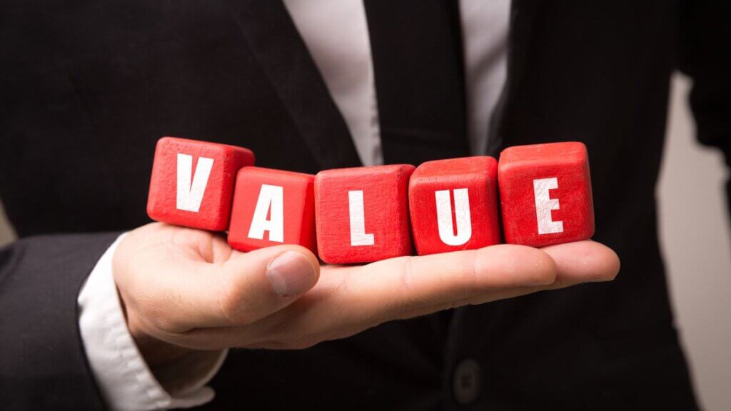 A hand holding red blocks spelling out "VALUE".
