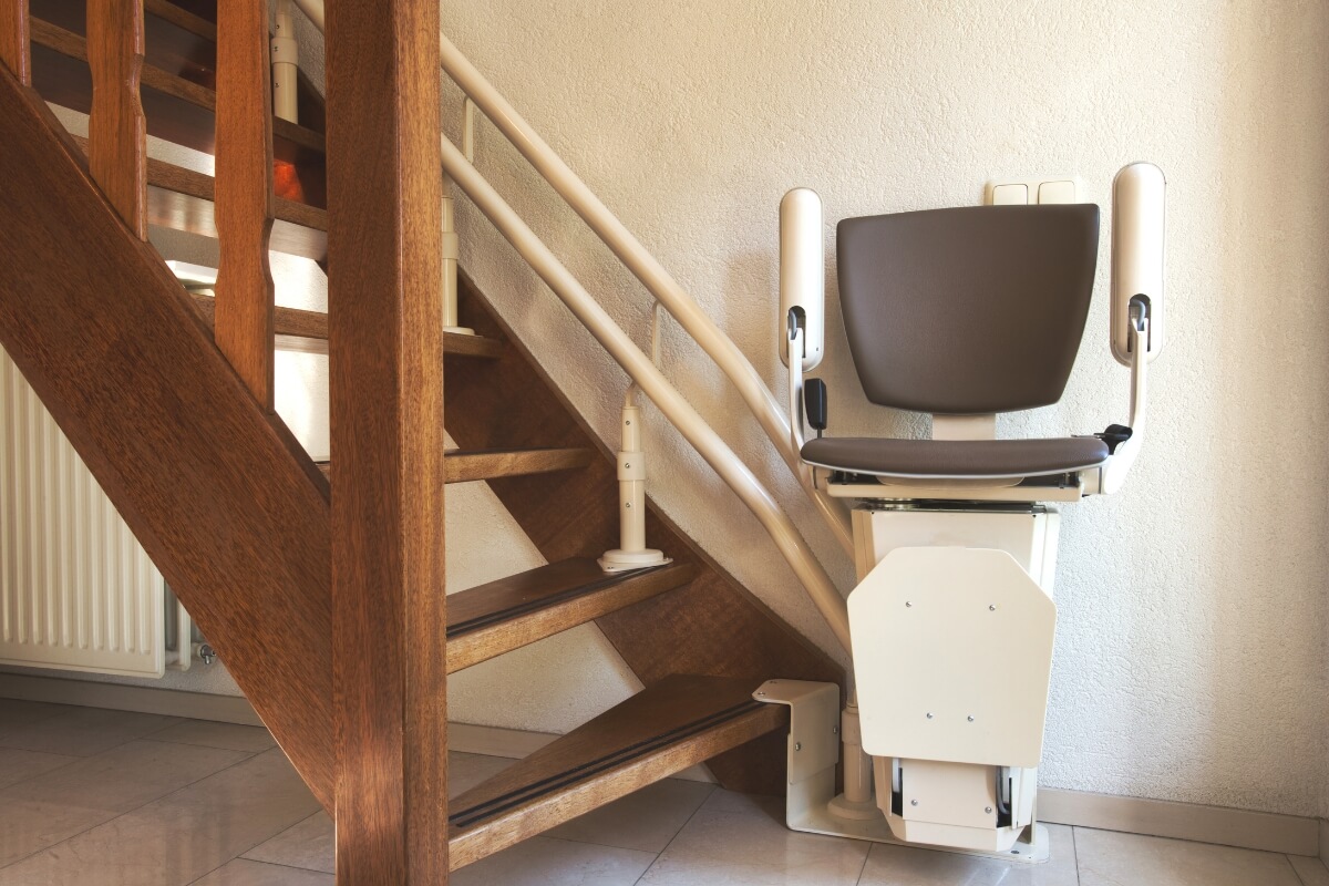 A close-up view of a dark grey stairlift chair being installed onto white dual rails along a wooden staircase.