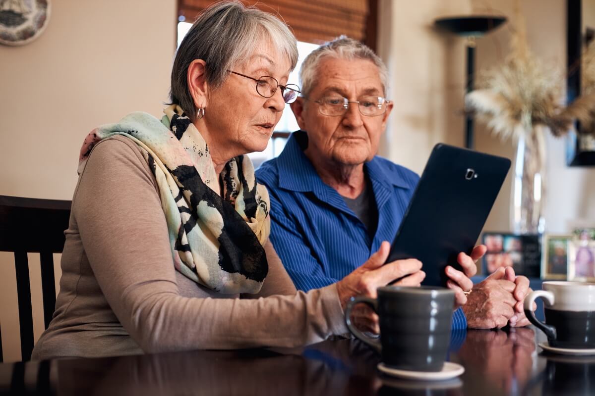 An older couple sitting at a table looking at a tablet together.