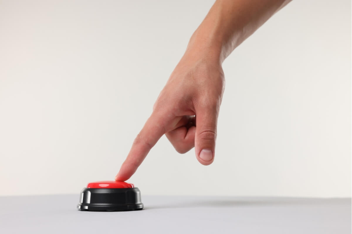 A hand reaching down to press a large red button.