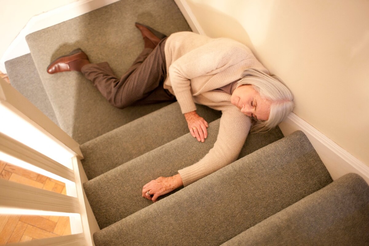 An older adult lying down on carpeted stairs after a fall.