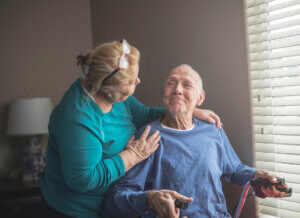 An elderly woman leaning in to talk to an elderly man who is using a walker and smiling.
