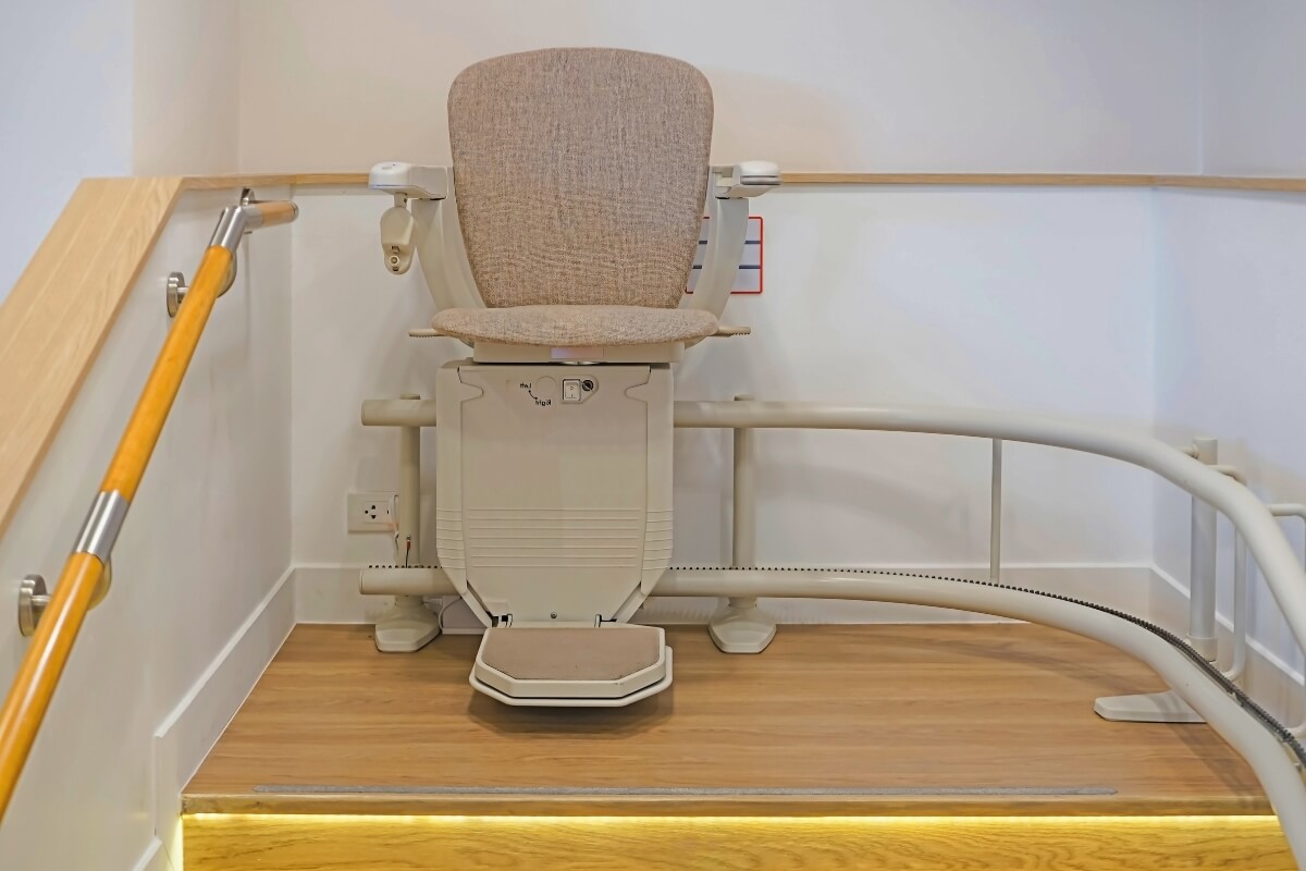 A close-up of a technician's hand using a screwdriver to perform maintenance or repairs on the motor housing of a stairlift at the base of a staircase.