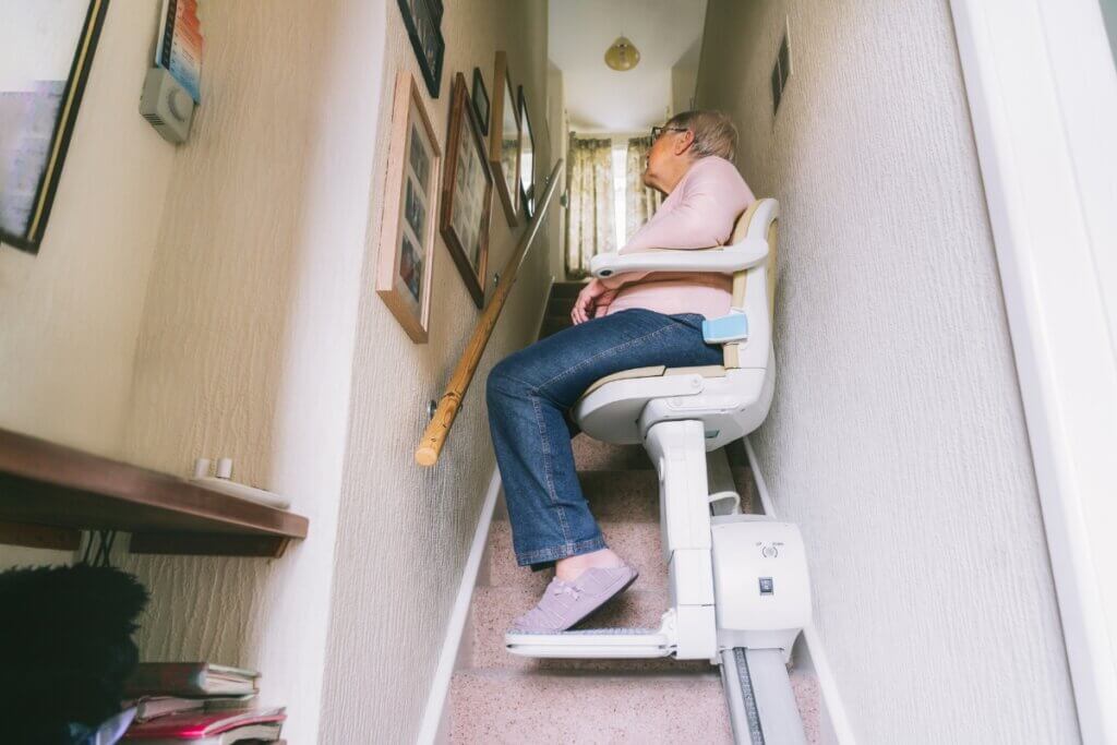 A person sitting in a modern stairlift, smoothly riding up a bright, contemporary staircase.