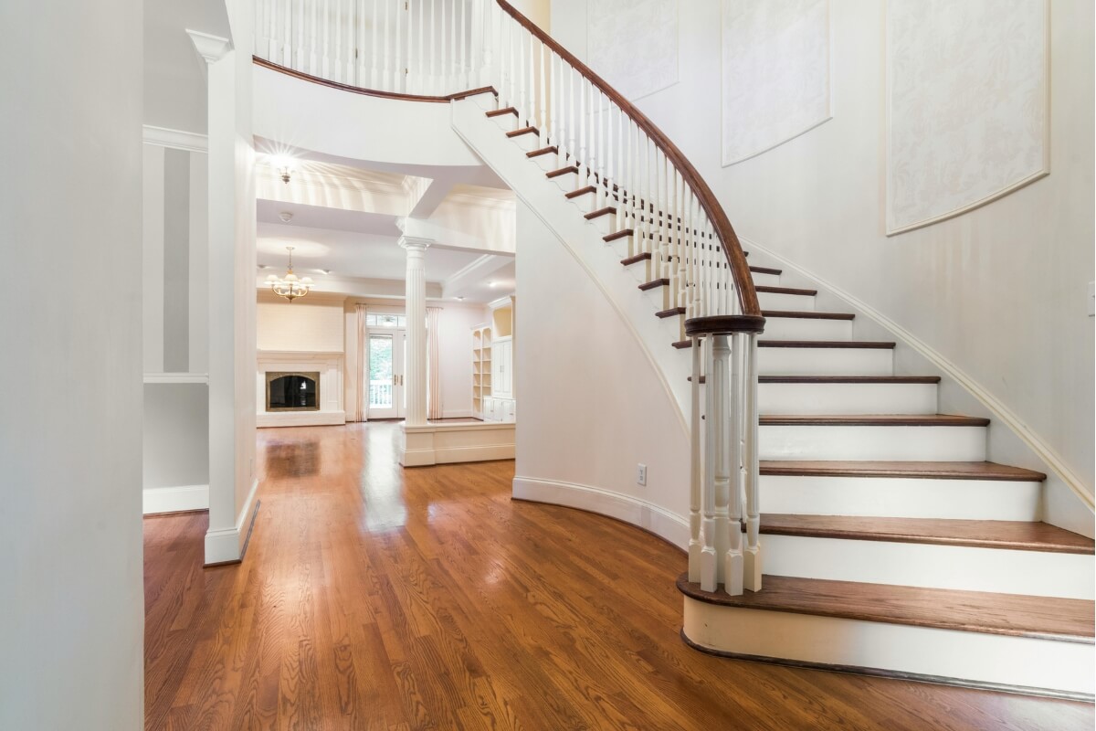 A curved stairlift parked at the bottom turn of a winding staircase, demonstrating a custom-fit rail.