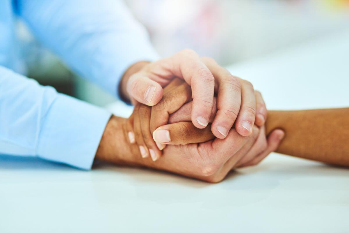 Close-up of two people holding hands across a table in a supportive, comforting gesture.