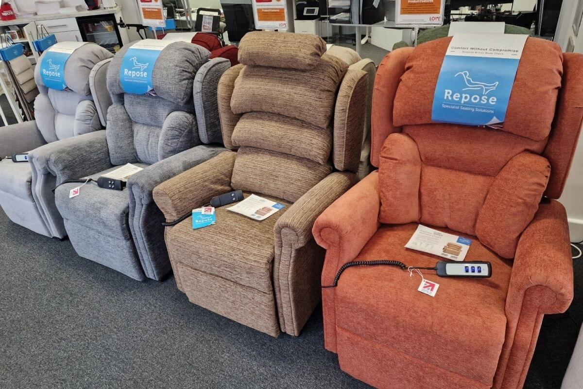 A showroom row displaying several upholstered power riser recliner armchairs in varying fabric shades.