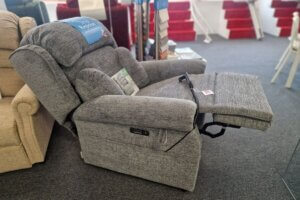 A grey fabric riser recliner chair shown in a semi-reclined position with the footrest extended inside a showroom.