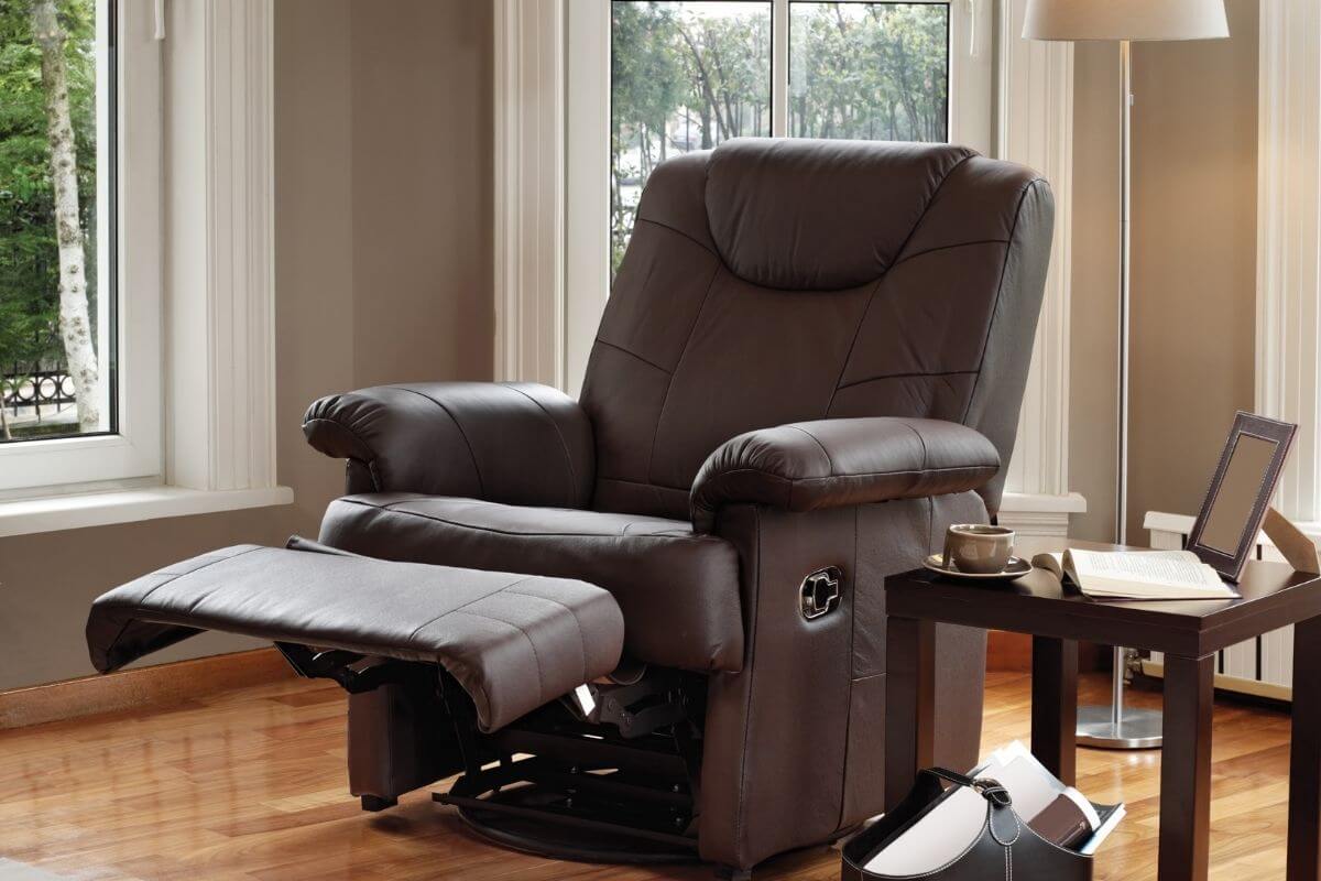 A dark brown leather recliner chair with its footrest extended, set next to a side table in a bright living room.