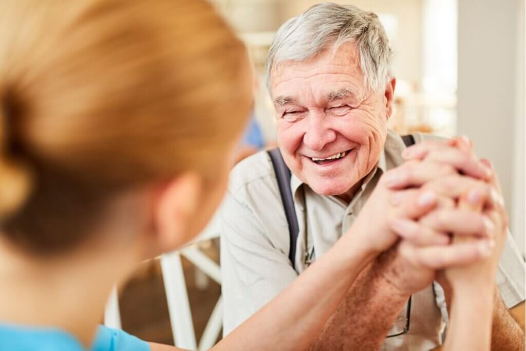 A smiling senior man clasping hands with a family member during a warm conversation about Mobility Challenges.